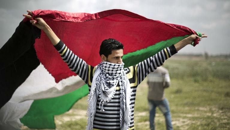 Un manifestante ondea una bandera palestina en la valla fronteriza entre Israel y la Franja de Gaza durante una protesta en 2014.
