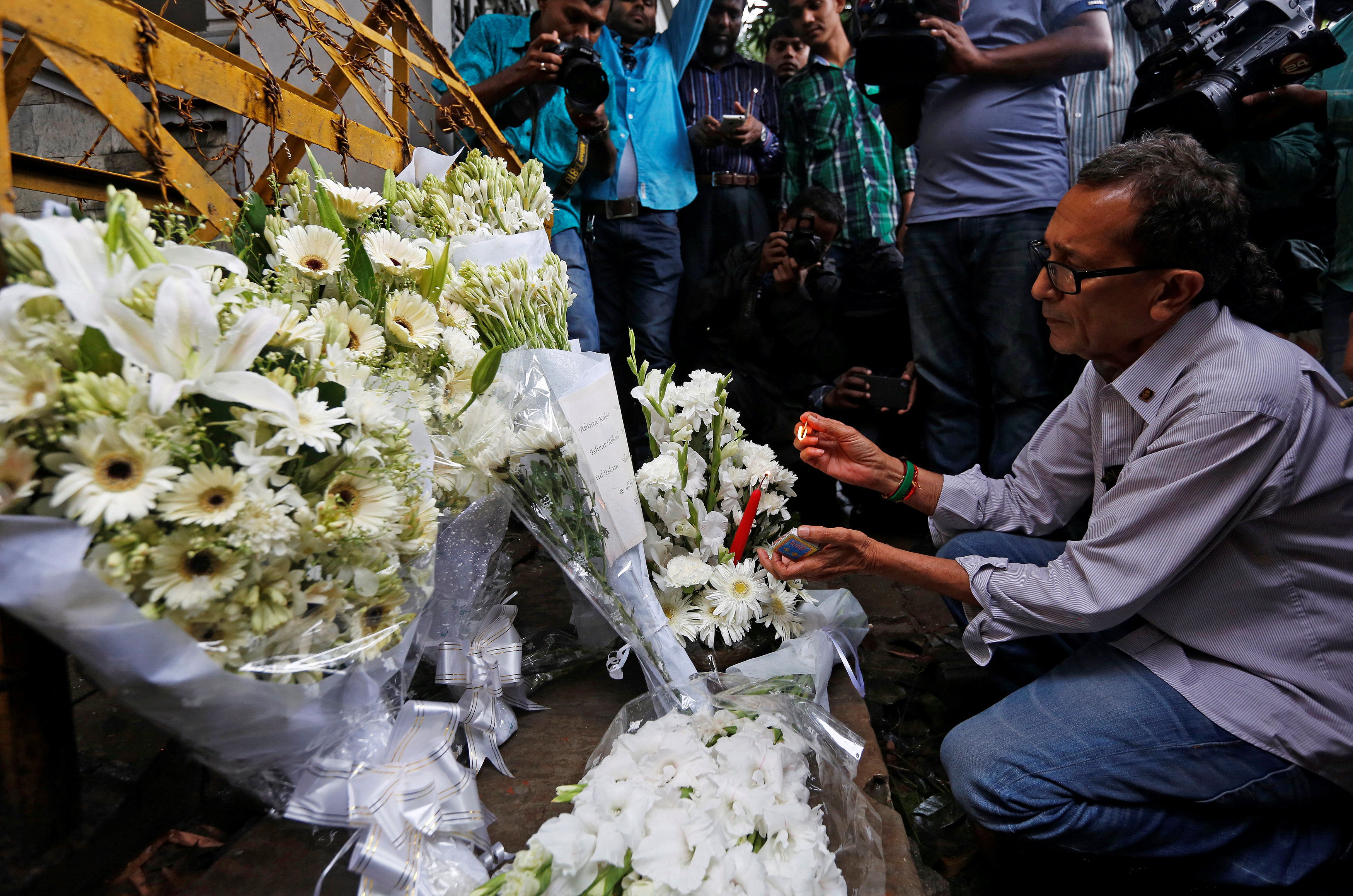 Un hombre enciende una vela en un monumento improvisado, para rendir homenaje a las víctimas del ataque a la Holey Panadería Artesanal y el Restaurante O'Kitchen.