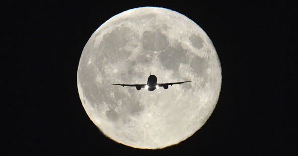 A plane flies in front of the moon.