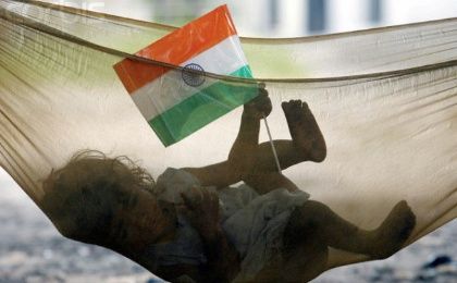 Indian child plays with Indian national flag while lying in hammock in a slum in Chandigarh, India. 