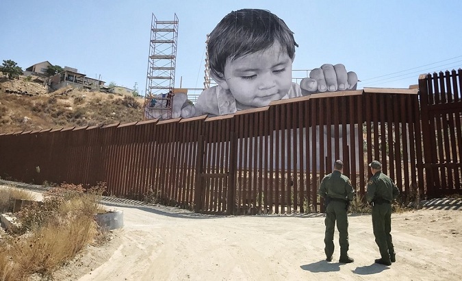 The boy glances down from the Mexican side at two Border Patrol officers in the United States.