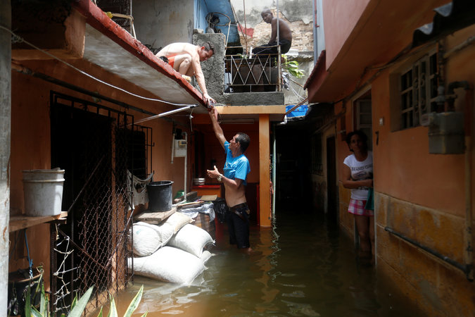 A man passes a drink to a neighbour while standing in the flooded passage of a block of flats