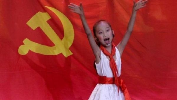 A schoolgirl performs in front of the flag of China's Communist party.