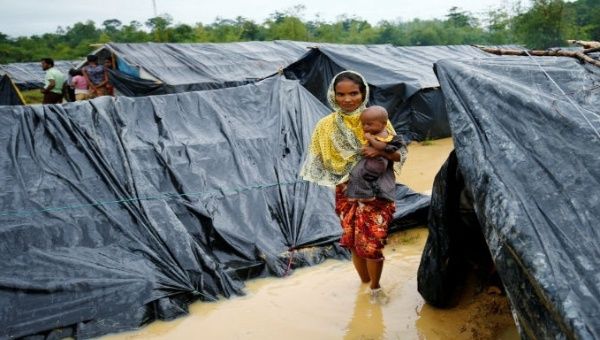 A Rohingya refugee woman and her child walk in floodwaters near makeshift shelters after heavy rains in Cox's Bazar, Bangladesh. 