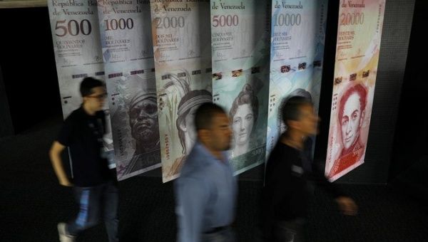 People walk by banners of Venezuelan bolivar notes displayed at the Venezuelan Central Bank building in Caracas, Venezuela.