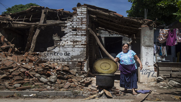 Una habitante de un municipio mexicano cocina junto a una vivienda destruida.