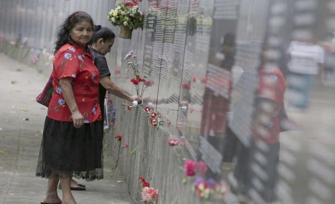 Two women place flowers at the Truth and Memory Monument to commemorate the dead and disappeared from the Salvadoran Civil War.