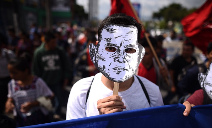 A protester wears a mask depicting Guatemala President Jimmy Morales during a large march.