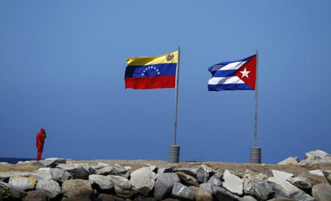 A worker stands next to Venezuelan and Cuban flags in a beach in La Guaira, in the state of Vargas outside Caracas.