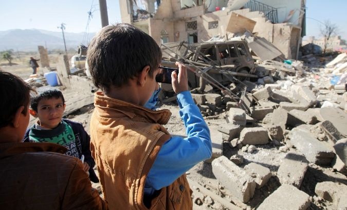 A boy takes a picture of a house laid to rubble by Saudi aerial shelling.