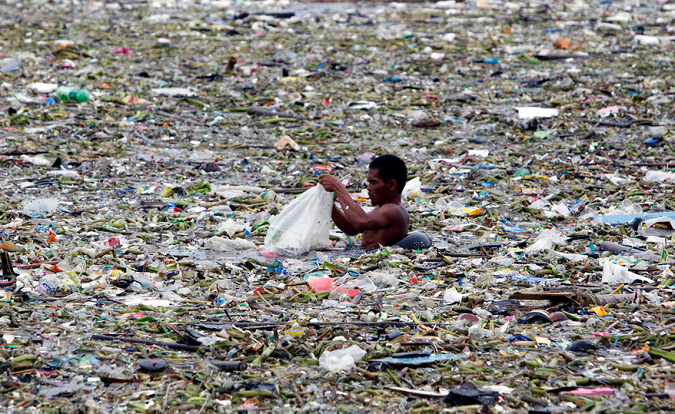 A man collects plastic and other recyclable materials from debris in the waters of Manila Bay in Manila, Philippines, July 30, 2012. Mismanaged waste from land is the primary cause of the ocean plastics crisis.