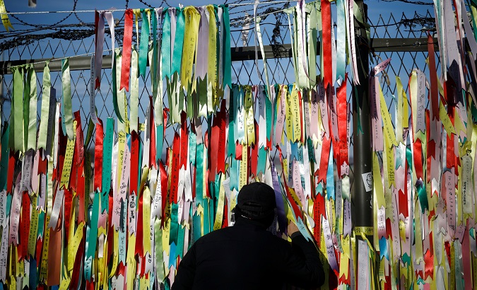 A man peeps through a barbed-wire fence decorated with ribbons bearing messages wishing for the unification between the two Koreas near the demilitarized zone.