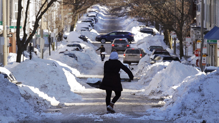 Una persona (c) carga una pala llena de nieve hacia una pila mientras trata de abrirle camino a su automóvil en Boston.