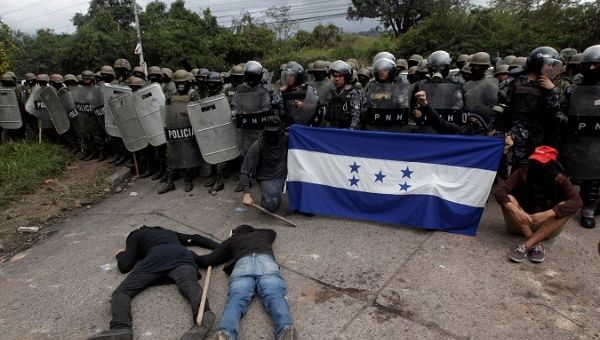 Opposition supporters hold a Honduran flag as others lie on the floor in front of security forces during post-electoral protest.