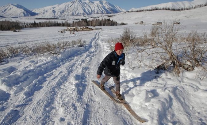 A young boy makes his way on horse-hide skis.