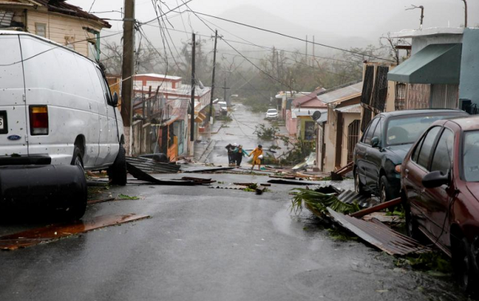 People walk on the street next to debris after the area was hit by Hurricane Maria in Guayama, Puerto Rico.