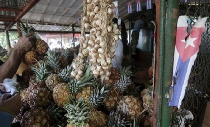 A Cuban flag hangs near pineapples and onions at a state market in Havana.