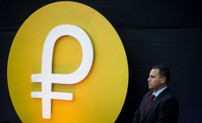 A Venezuelan security official stands in front of the Petro cryptocurrency logo.