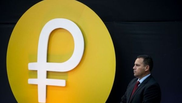 A Venezuelan security official stands in front of the Petro cryptocurrency logo.