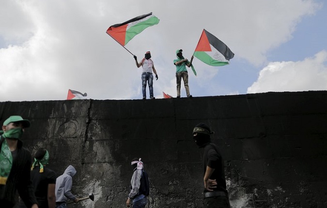 Palestinian protesters wave Palestinian flags on the Israeli barrier separating the West Bank town of Abu Dis from Jerusalem, during clashes with Israeli troops Oct. 28, 2015.