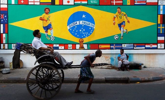 A rickshaw transports a passenger past a mural of Brazil's Neymar and Marcelo in India.