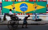 A rickshaw transports a passenger past a mural of Brazil