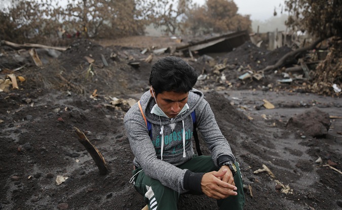 A resident sits on the rubble as people continue to search for remains of victims after the eruption