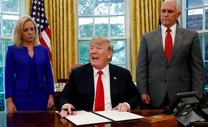 U.S. President Donald Trump (C) signs an executive order to keep migrant families together as they enter the United States.