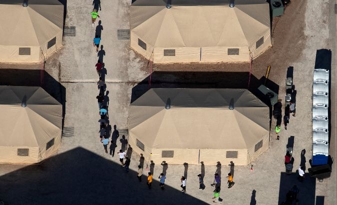 Immigrant children are led by staff in single file between tents at a U.S. detention facility.