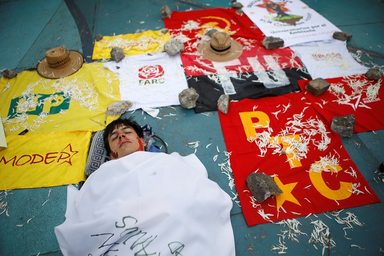 A protester appears lifeless next to the flags of political parties that have been targeted by conservative forces and right-wing paramilitaries.