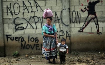 A Mayan indigenous woman and her son in front of a graffiti that reads 