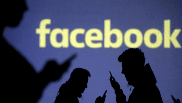Silhouettes of mobile users are seen next to a screen projection of Facebook logo. March 28, 2018