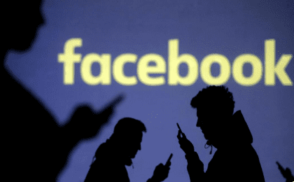 Silhouettes of mobile users are seen next to a screen projection of Facebook logo. March 28, 2018