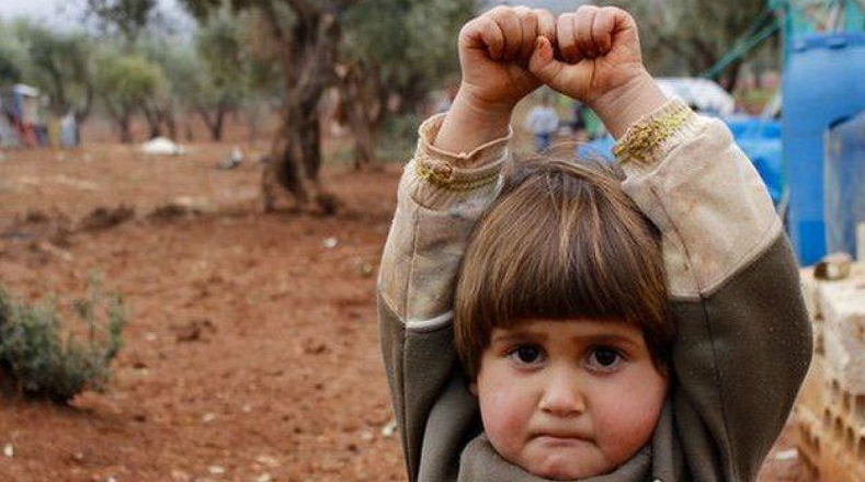  Esta niña siria alza sus brazos en señal de rendición cuando es enfocada por el lente de un camarógrafo para ser fotografiada. La imagen reflejar la violencia que han vivido los niños sirios por causa de los ataque del autodenominado Estado Islámico.