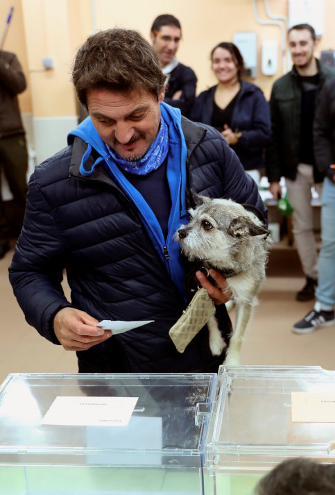 Un elector acompañado de su mascota deposita el sobre con las papeletas en una urna en la localidad de Galapagar, en Madrid.