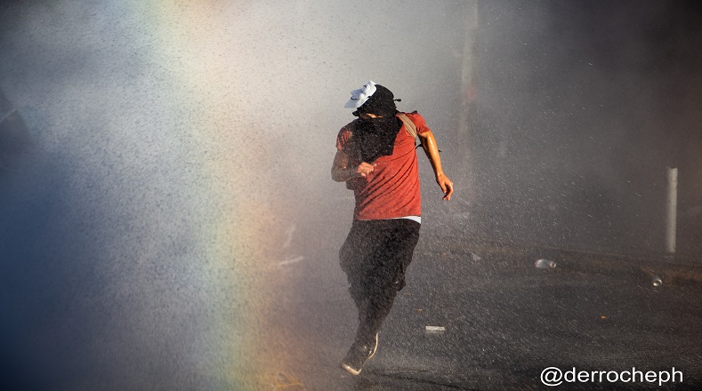 Encapuchado corriendo para no ser alcanzado por el chorro de agua del vehículo policial (Santiago de Chile, 31 de octubre de 2019).