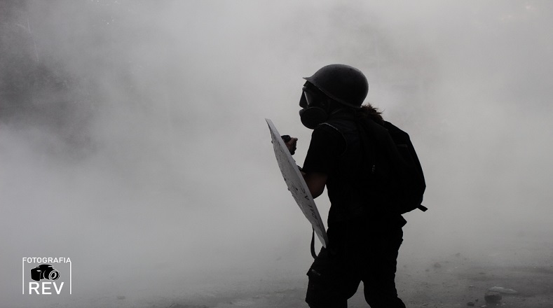 Escudero de primera linea observa a las fuerzas policiales bajo la nube del gas lacrimogeno. Plaza Baquedano (Santiago de Chile, 04 de noviembre de 2019).