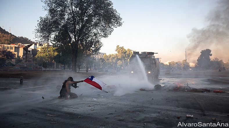 Manifestante afectado por quimicos del huanaco (carro lanza agua) es vuelto a impactar con su chorro de agua. Plaza de la dignidad (Santiago de Chile, 9 de noviembre de 2019).