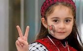 Girl with Palestinian flag painted on her face makes victory sign.