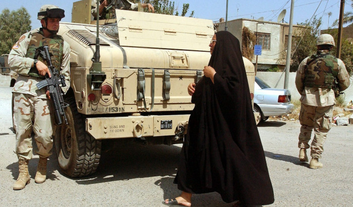 Fotografía tomada en septiembre de 2004 que muestra a una mujer iraquí que se cruza con soldados estadounidenses que patrullan las calles de Bagdad, Irak.
