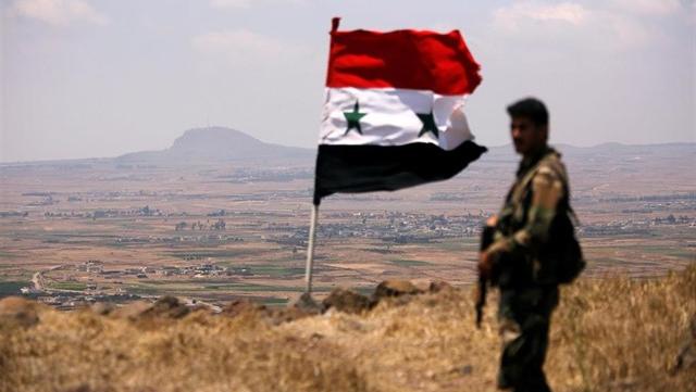 Soldado sirio junto a la bandera nacional.