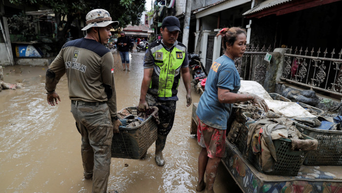 Residentes llevan sus pertenencias mientras limpian su casa en una zona afectada por las inundaciones en Indonesia.