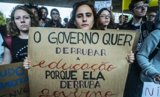 Woman holds a sign that reads ‘The government wants to overthrow education because education overthrows the government’.