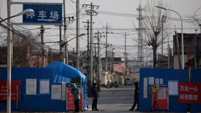 Voluntarios de seguridad pública usan cubrebocas mientras hacen guardia en la entrada de una comunidad rural de China.