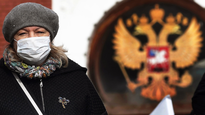 Una mujer con mascarilla camina junto a un Escudo de armas de Rusia en Moscú.
