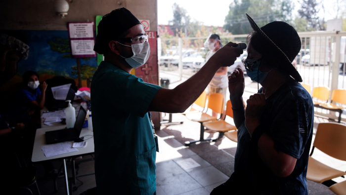 Un enfermero le toma la temperatura a una mujer a la entrada de un centro de salud en Santiago de Chile.