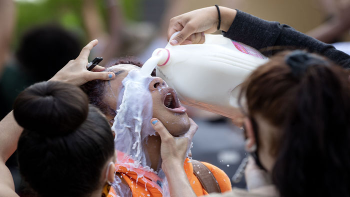Personas asisten a una mujer afroamericana arrojando leche sobre su ojos, intentando calmar el ardor causado por el gas lacrimógeno proveniente de la represión policial en Minnesota. 