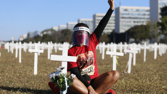 Una activista porta una mascarilla y careta mientras permanece sentada entre cruces colocadas simbolizando a las personas que han fallecido por la Covid-19 en Brasil.