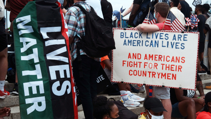 Un hombre sostiene un cartel junto a una persona envuelta en una bandera de 'Black Lives Matter' durante una marcha en Washington, D.C.